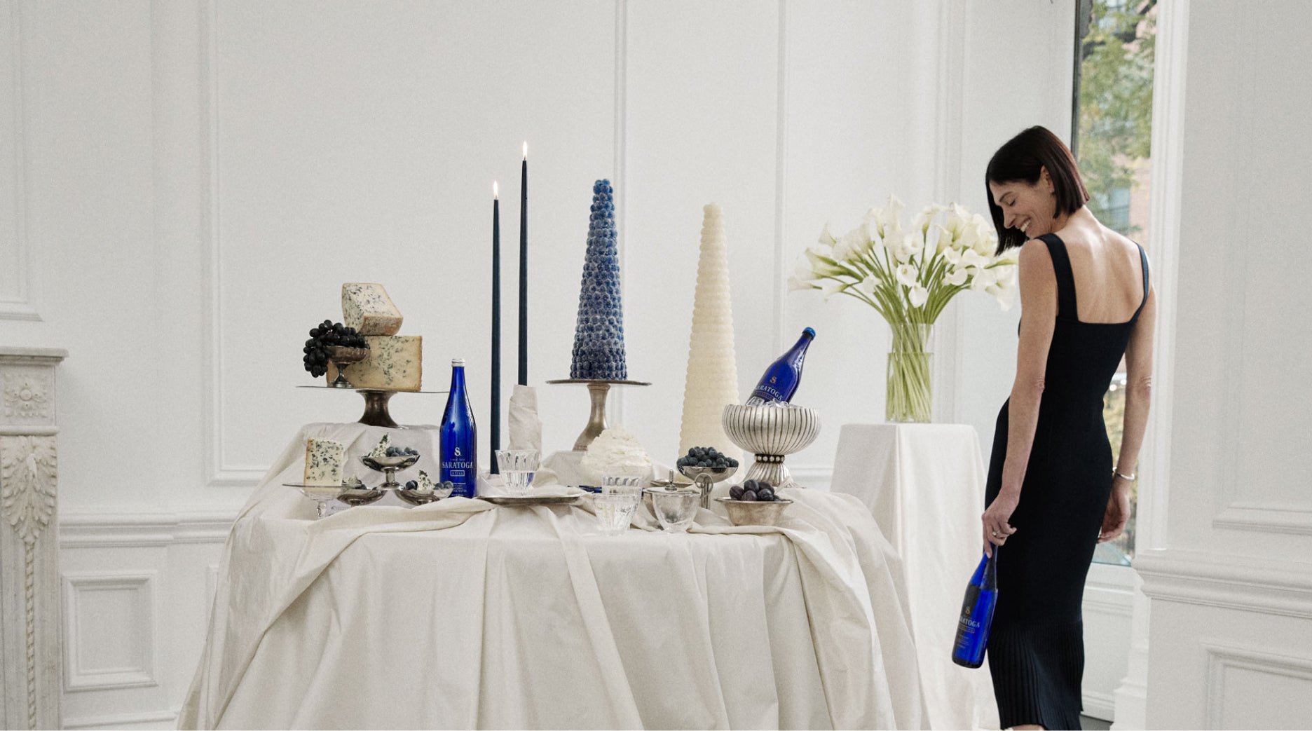 athena calderone wearing a black dress standing by a table filled with desserts and saratoga spring water