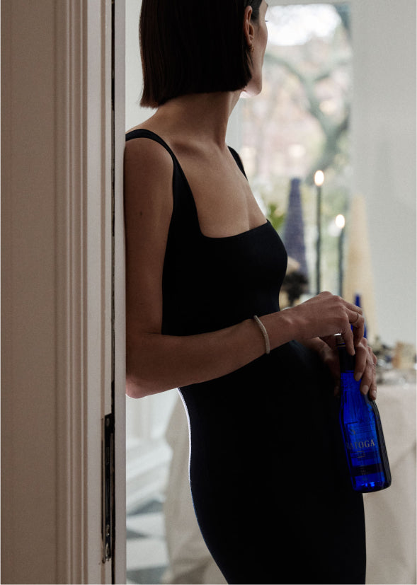woman in a black party dress standing in a doorway holding a blue bottle of saratoga spring water