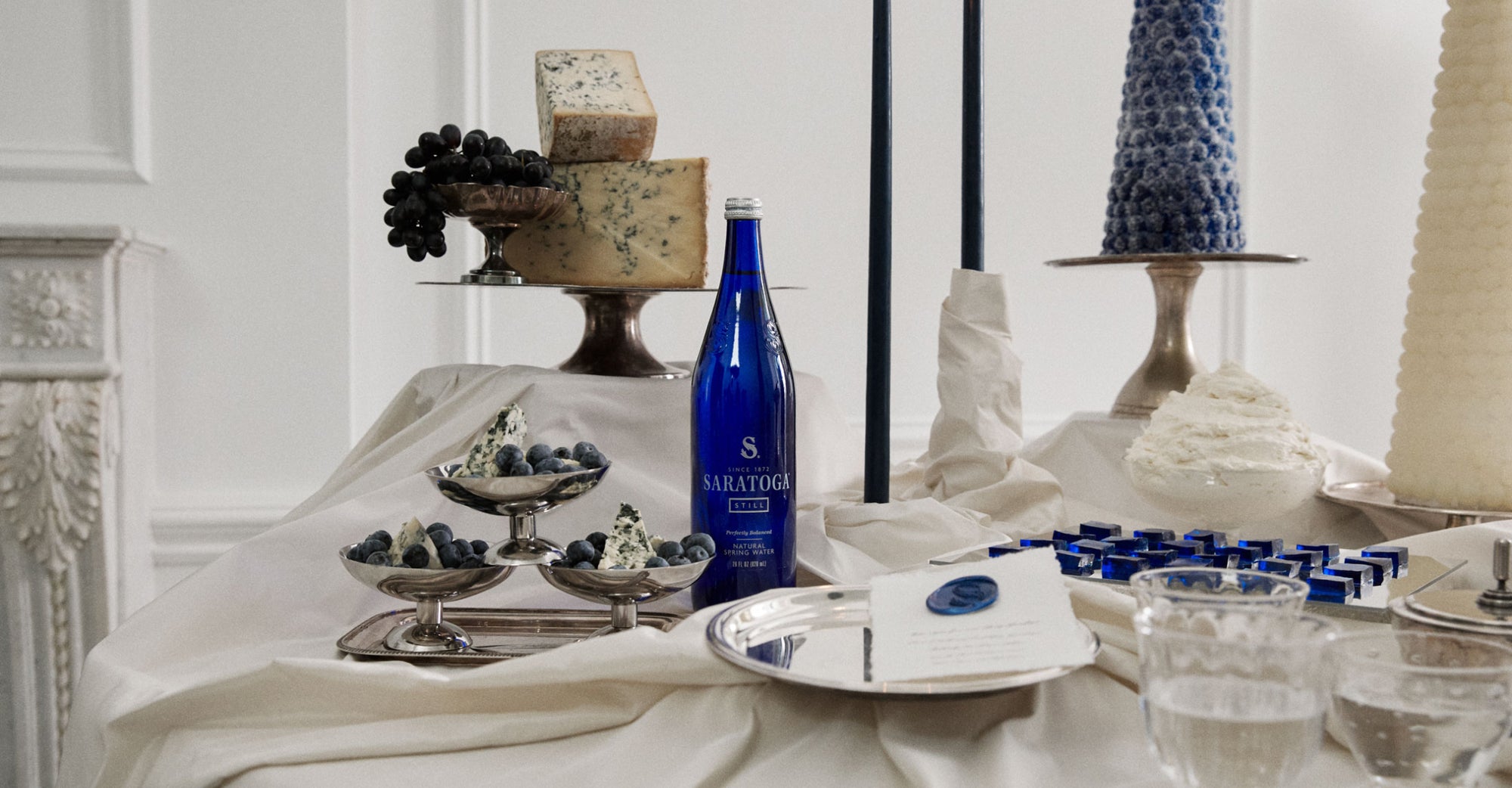 antique silver serving trays holding blue cheese and concord grapes and blueberries among other desserts and a bottle of saratoga spring water