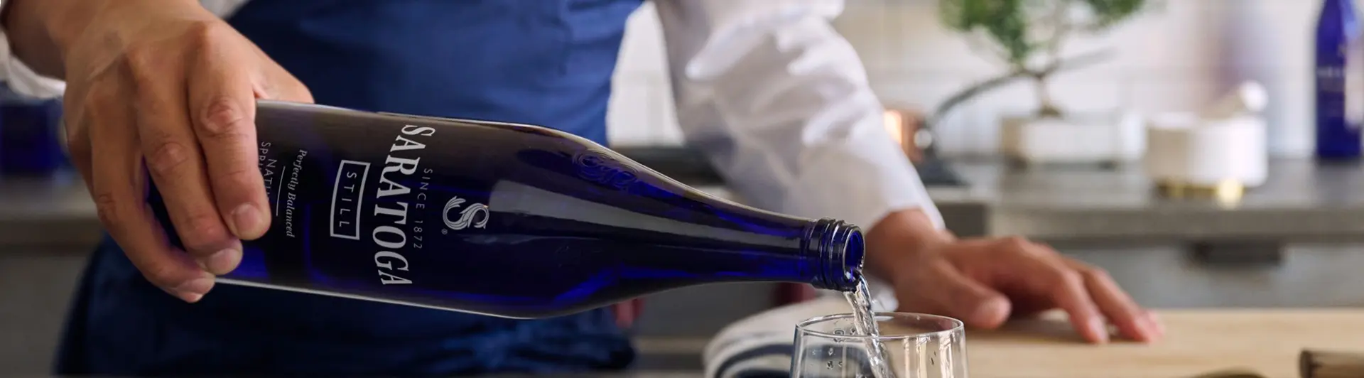 A chef in a blue apron pours a bottle of Saratoga Spring Water.